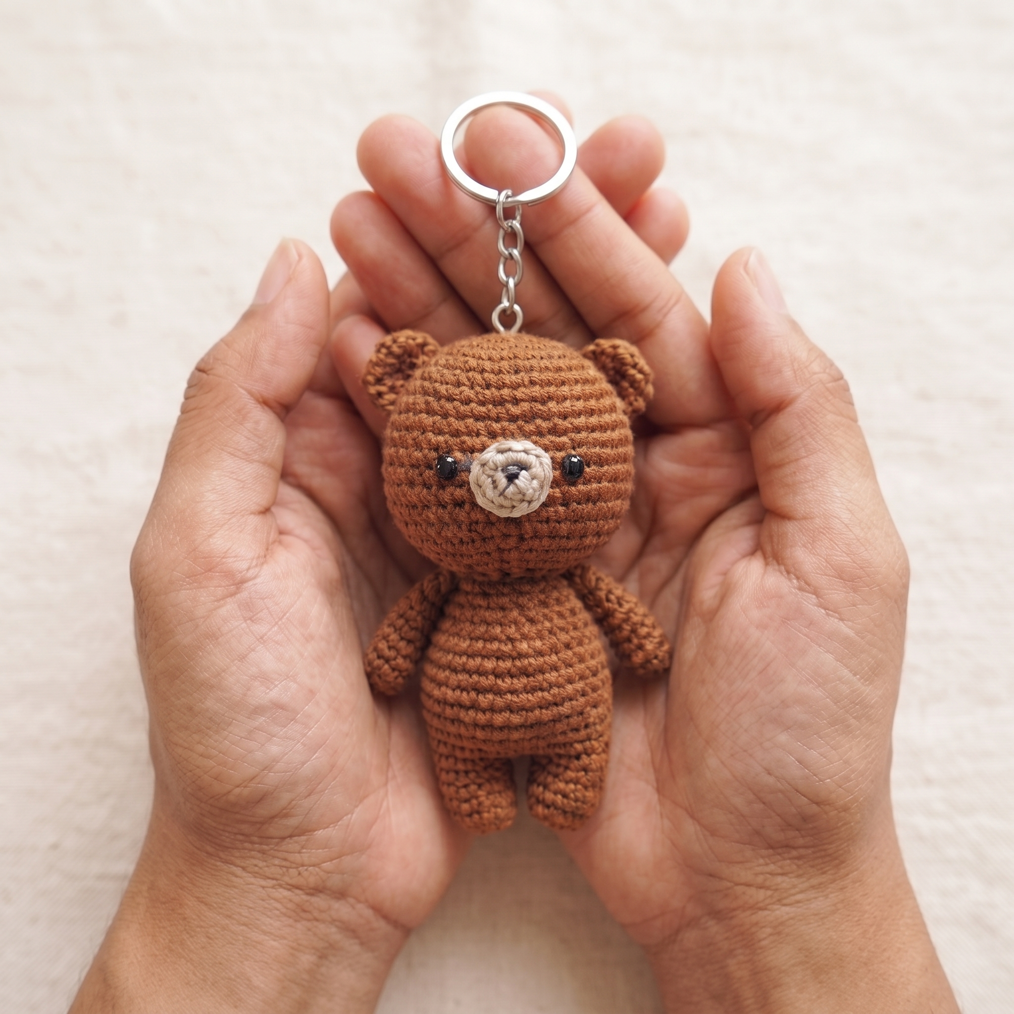 Tiny crochet teddy bear amigurumi keychain held in the palm of a hand
